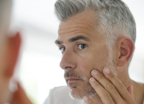 Middle-aged man inspecting his face, mirror view