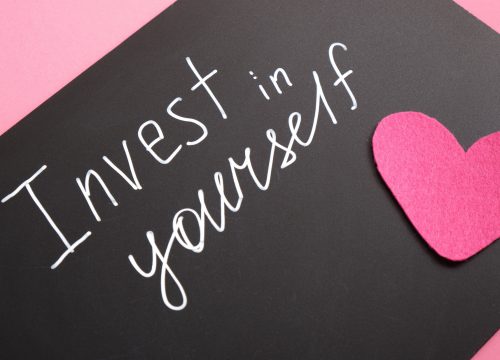 Invest In Yourself written in chalk on a blackboard with a paper cutout of a heart