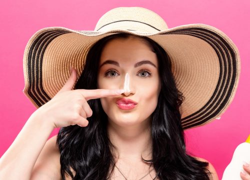 Young woman holding a bottle of sunblock on a solid background