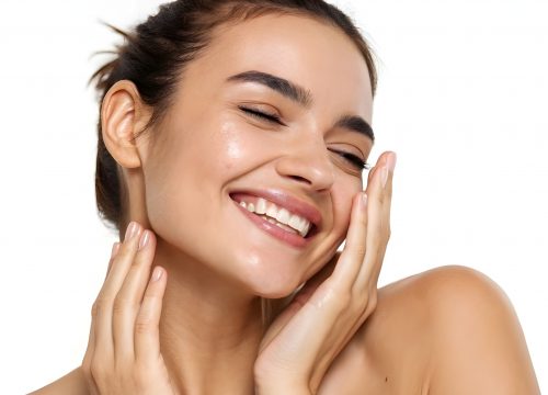 A smiling woman with glowing skin gently touches her face, eyes closed.