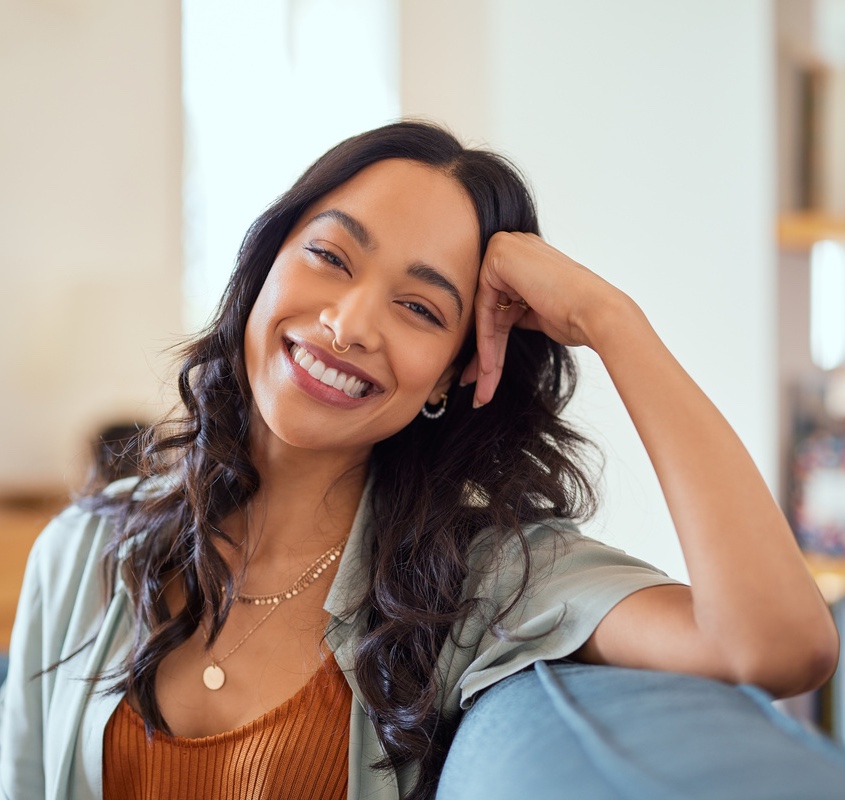 Portrait of happy young latin woman sitting on sofa at home while looking at camera. 
